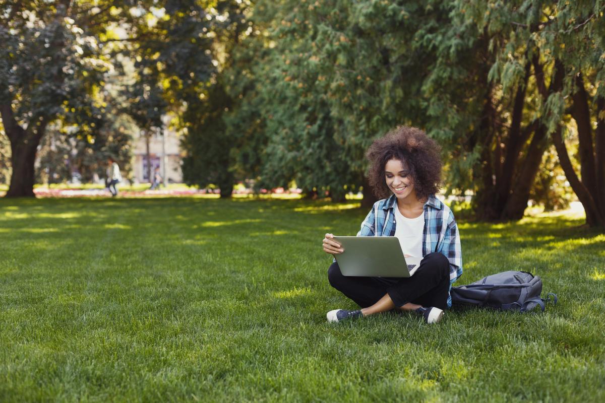 Young woman sitting on grass with laptop