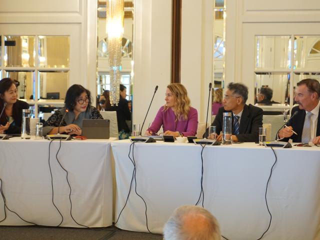 Five panelists speaking at a white table with microphones