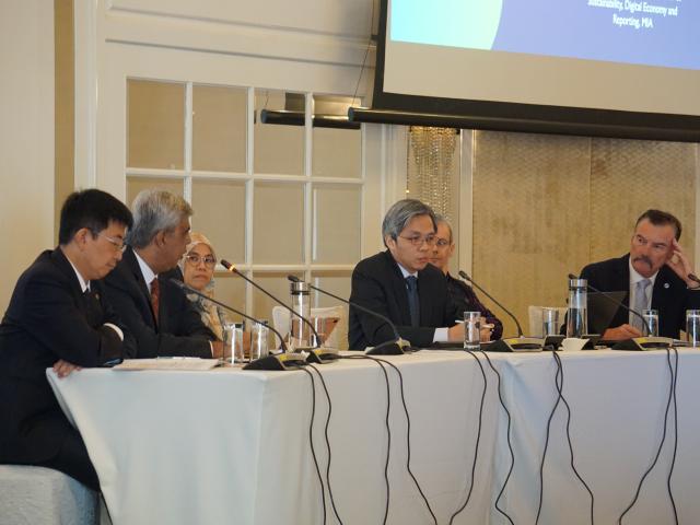 A panel of six people discussing at a white table with microphones