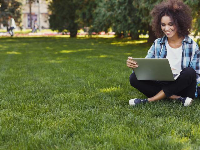 Young woman with laptop sitting on grass