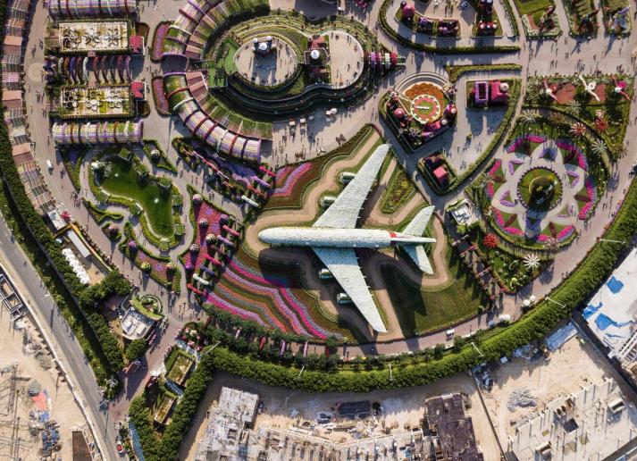 A manicured park with pink flowers and a hedge shaped like a to-scale airplane