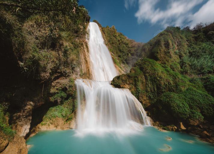 A waterfall emptying into a blue pool. surrounded by a forest