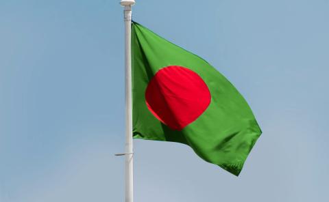 The flag of Bangladesh waving outside over a blue sky