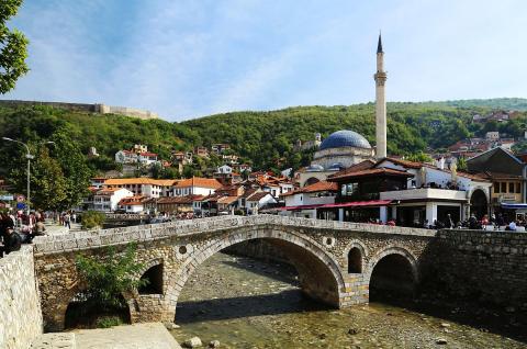 A stone bridge over a creek in a village with a stone tower and red roofs