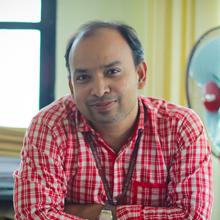 A man in a red plaid shirt, smiling at the camera