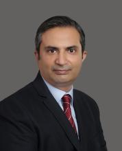 Portrait of a man with a dark suit and red tie, turning to look at the camera