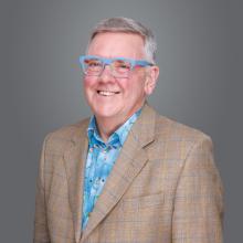 A man standing wearing a tan jacket and light blue glasses