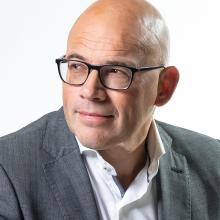 Headshot of a man wearing glasses and a white button down and gray jacket